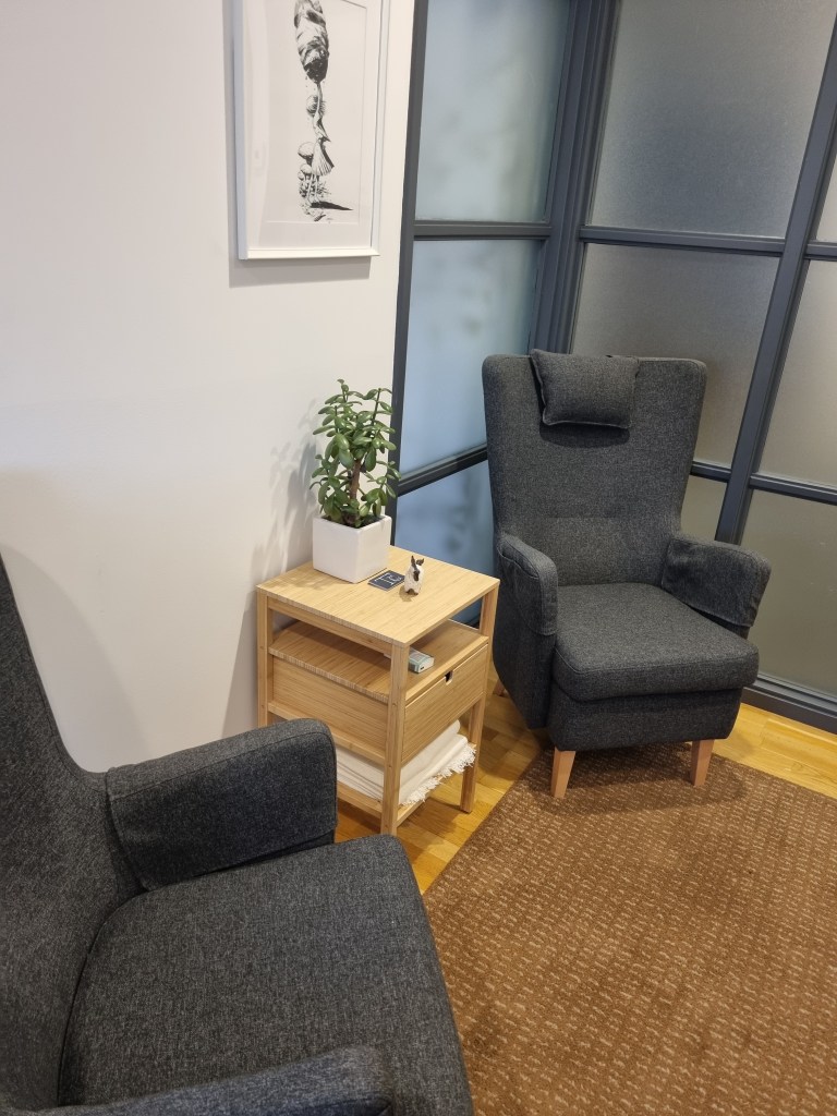 Två bekväma stolar, däremellan ett avställningsbord med en planta och en figurin och en tavla ovanför