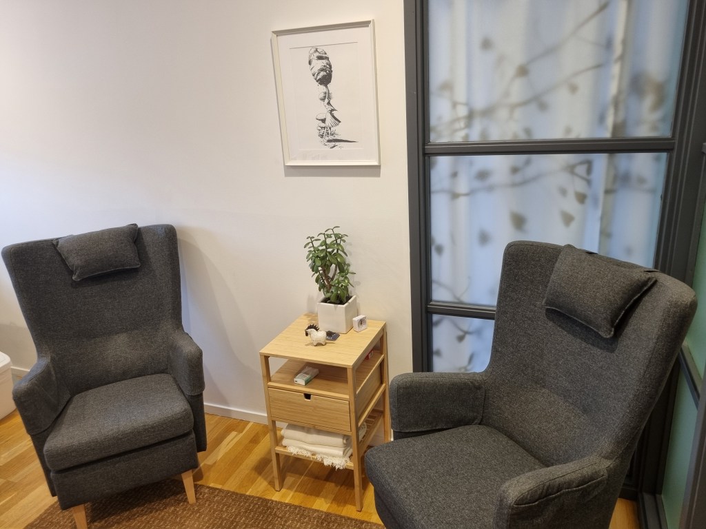 Två bekväma stolar, däremellan ett avställningsbord med en planta och en figurin och en tavla ovanför